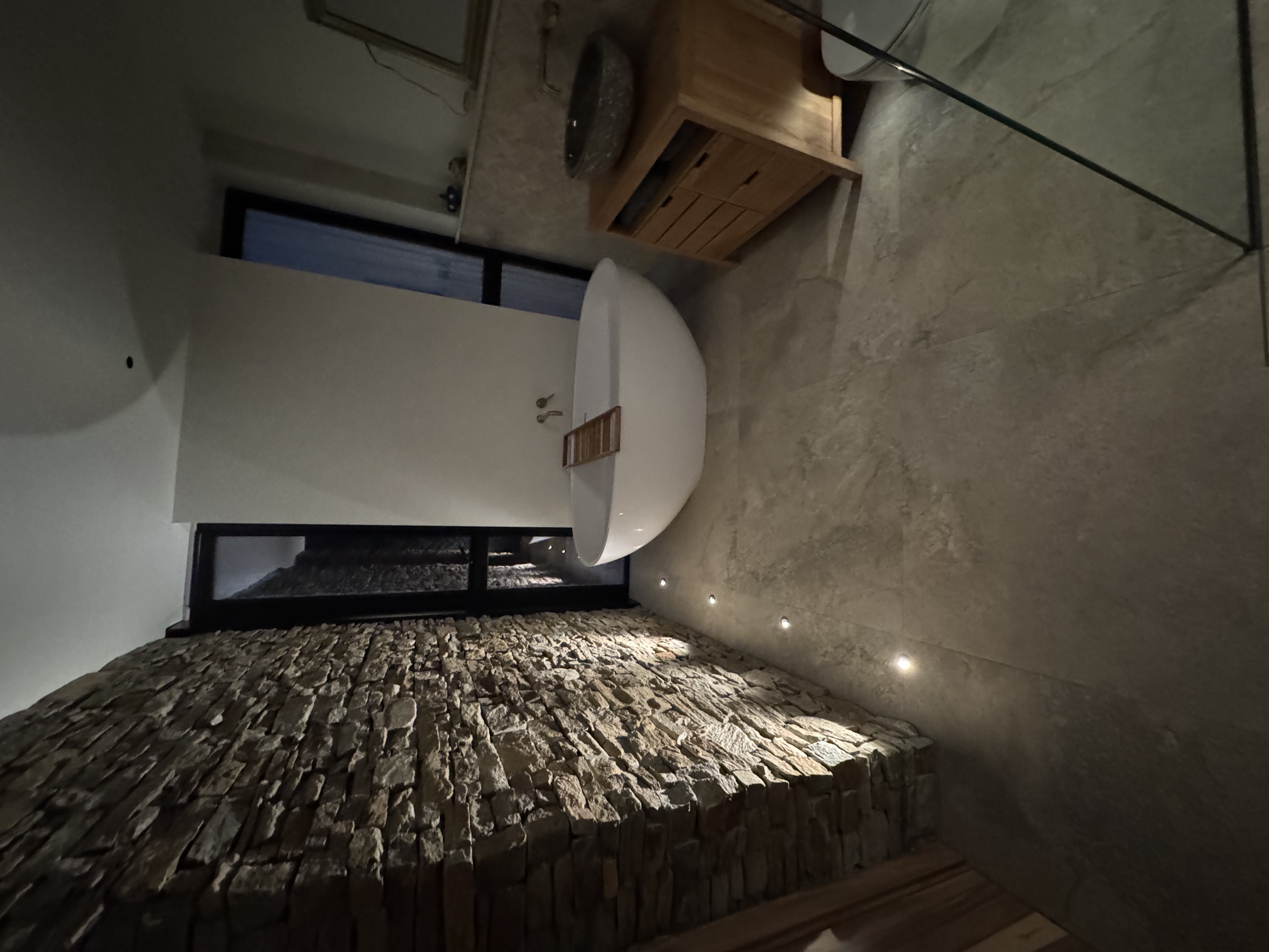 Recessed floor spotlights uplighting a natural stone feature wall beside a freestanding bath — bespoke lighting installation